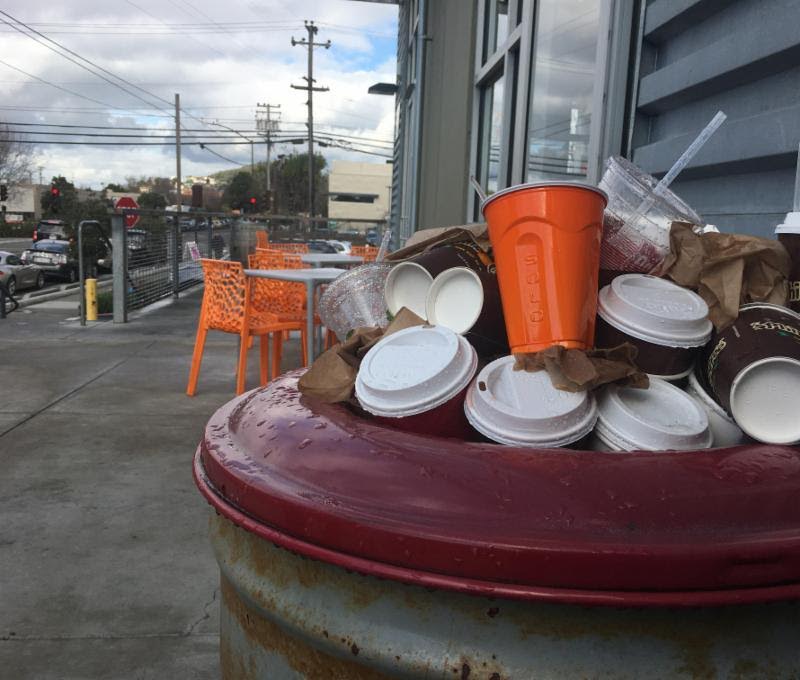 Overflowing trash bin with single-use-plastics in front of a shop