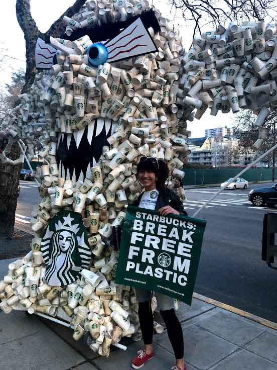 Lauren Moore stands beside a Plastic Monster while holding a sign of Break Free From Plastic