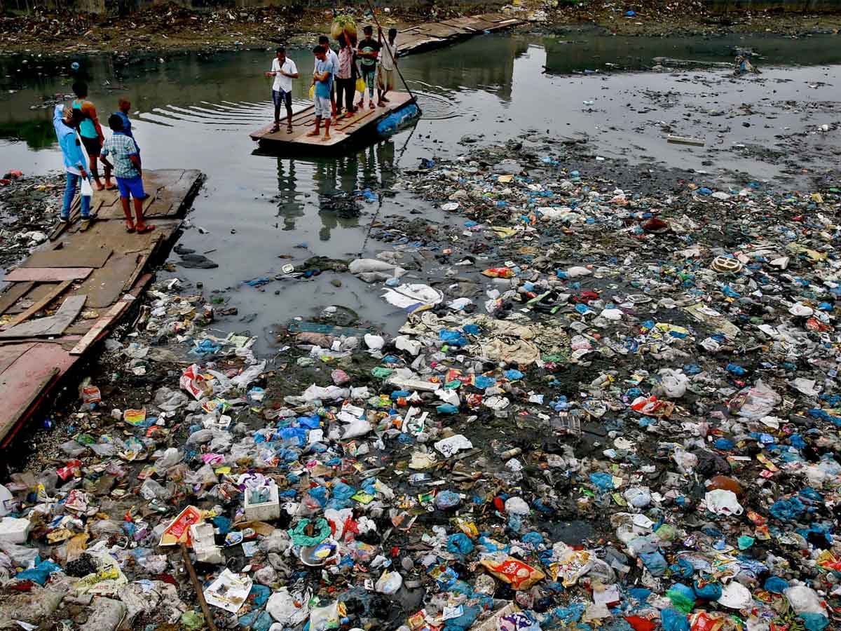 A group of people are crossing a river full of garbage in Mumbai, India