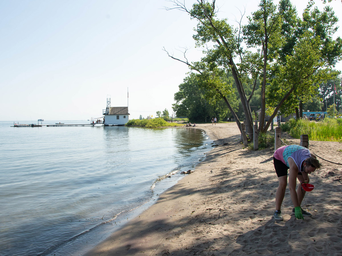 A view of the shoreline at Cherry Beach. A volunteer from a past cleanup bends down to pick up litter on the beach.