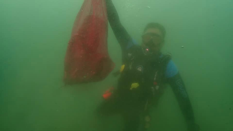 A diver is holding a large, red plastic bag underneath the ocean during the #BrandAudit2019 in Davao del sur, Philippines.