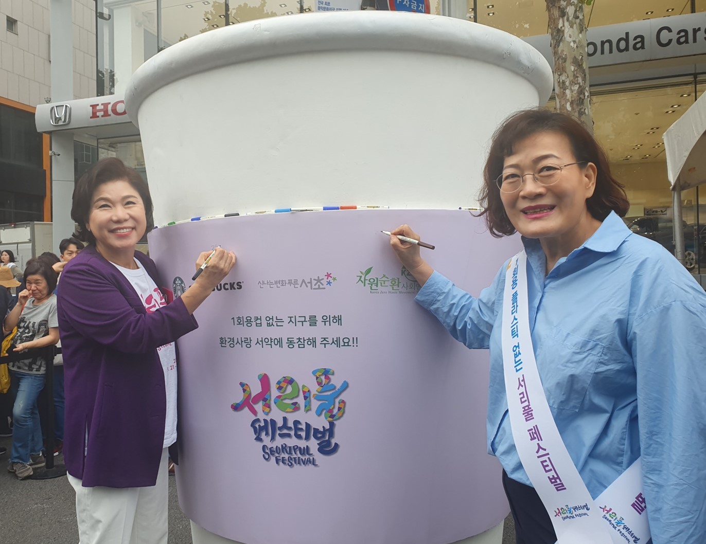 Two Korean women signing on a big reusable cup during the Seoripul Festival held in Seoul