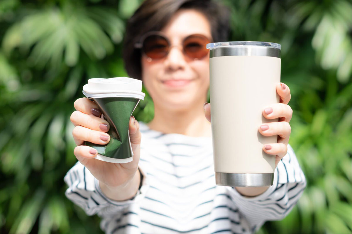 A woman holding a single-use coffee cup on her right hand and a glass of milk on her left hand.